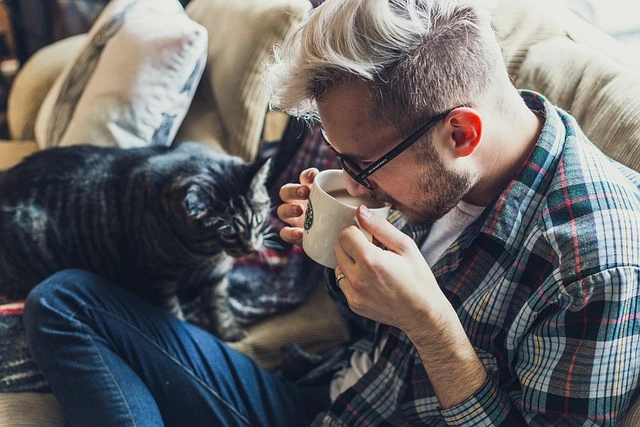 A man drinking coffee with a cat beside